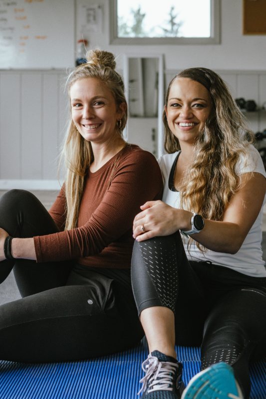 Two women sitting on a mat after a workout